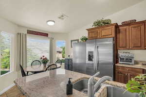 Kitchen with stainless steel fridge with ice dispenser, light stone counters, light tile patterned floors, and wood finish cabinets