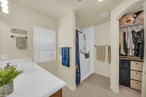 Bathroom featuring light carpet, a walk in closet, a shower stall, and vanity
