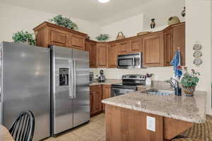 Kitchen featuring wood finish cabinetry, stainless steel appliances, light stone countertops, a peninsula, and light tile patterned floors