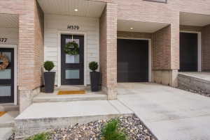 Entrance to home with cute front door and porch featuring an attached garage, driveway, and brick siding