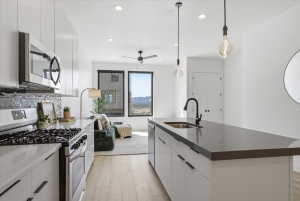Kitchen featuring stainless steel appliances, modern cabinets, white cabinetry, light wood-style floors, and an island with sink