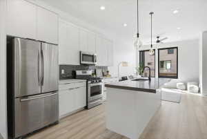 Kitchen with stainless steel appliances, white cabinets, a kitchen island with quartz counter tops sink, and light wood finished floors and incredible natural light for day and modern light fixtures for night.