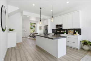 Kitchen with a center island with sink, white cabinets, stainless steel appliances, and light wood-style floors
