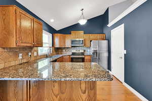 Kitchen with stainless steel appliances, lofted ceiling, dark stone counters, light wood-style flooring, and wood finish cabinets