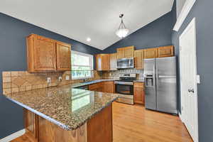Kitchen featuring stainless steel appliances, light wood-style floors, a peninsula, dark stone countertops, and lofted ceiling