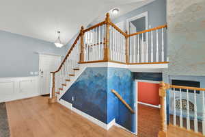 Stairs featuring a decorative wall, wood finished floors, and a wainscoted wall