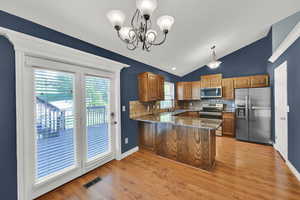 Kitchen featuring dark stone counters, stainless steel appliances, wood finish cabinetry, lofted ceiling, and tasteful backsplash