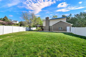 Back of house featuring brick siding, a fenced backyard, solar panels, a chimney, and a patio area