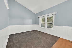 Spare room with a wainscoted wall, lofted ceiling, a decorative wall, and dark wood-style flooring