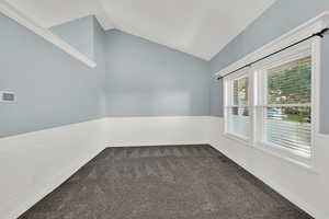 Empty room featuring wainscoting, dark colored carpet, vaulted ceiling, and a decorative wall