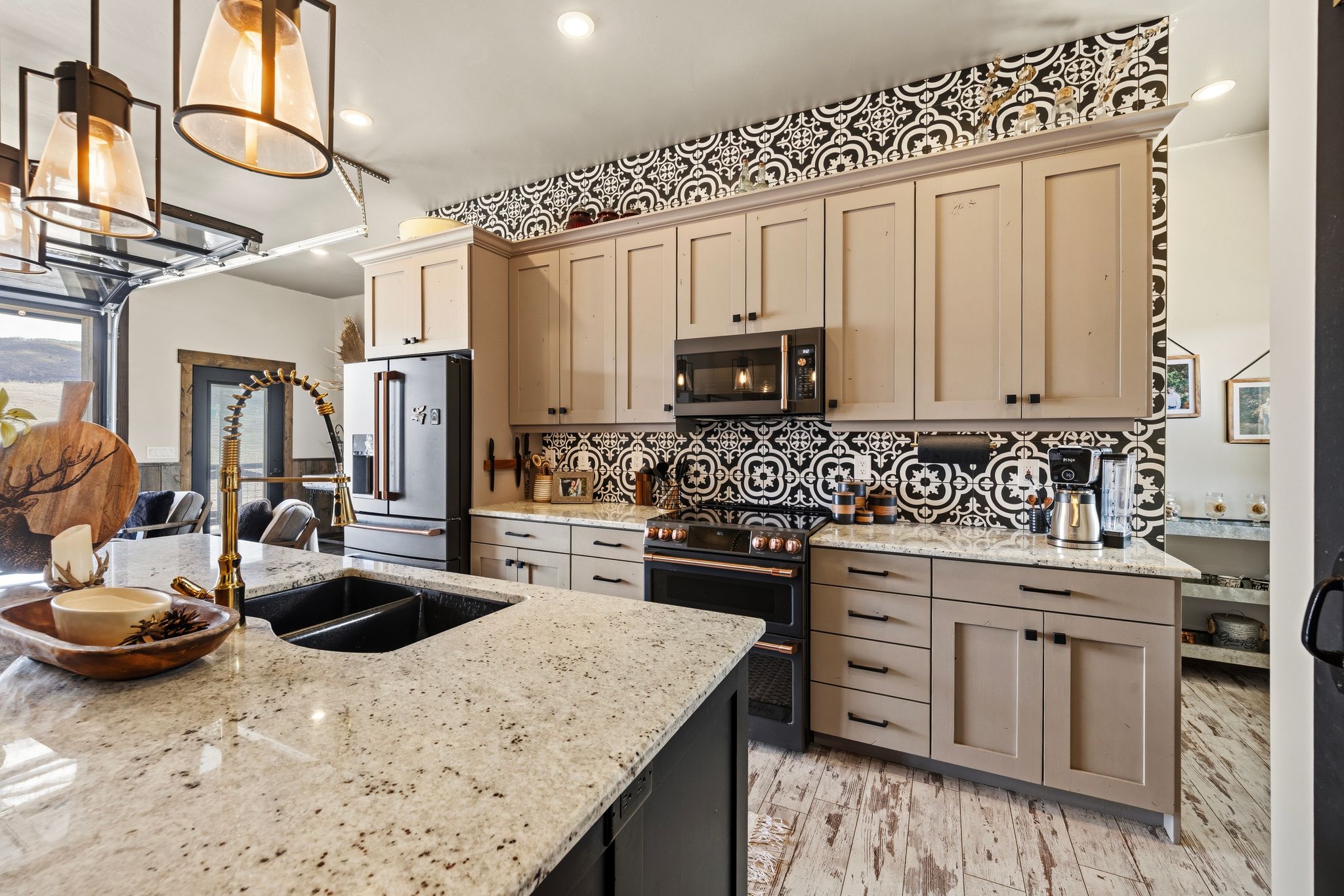 Dual tone kitchen featuring premium appliances, light stone counters, pendant lighting, light wood-style flooring, and tasteful backsplash