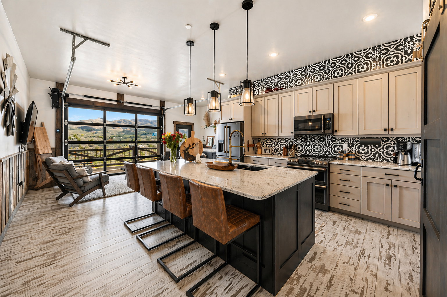 Dual tone kitchen featuring a kitchen bar, light stone counters, a center island with sink, stainless steel appliances, and hanging light fixtures