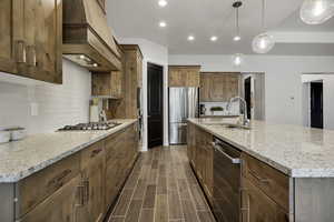 Kitchen featuring a large island, light stone countertops, wood finish floors, stainless steel appliances, and wood finish cabinets