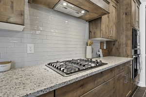 Kitchen featuring light stone countertops, stainless steel appliances, tasteful backsplash, and wood finish cabinetry