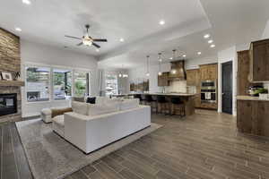 Living room featuring hanging lights, a ceiling fan, a stone fireplace, and wood tiled floors