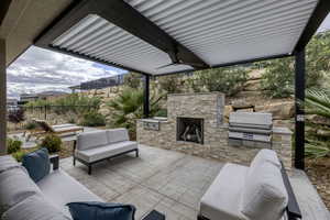 View of patio with an outdoor stone fireplace, a ceiling fan, and an outdoor kitchen with living area