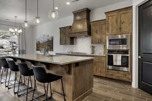 Kitchen featuring light stone countertops, stainless steel appliances, decorative backsplash, a breakfast bar, and a center island with sink
