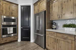 Kitchen with light stone counters, stainless steel appliances, tasteful backsplash, wood tiled floors, and wood finish cabinets
