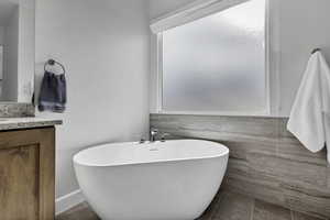 Bathroom with vanity, a freestanding tub, tile walls, and dark tile patterned flooring