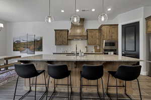 Kitchen with a breakfast bar area, light stone counters, wood finish cabinetry, a kitchen island with sink, and stainless steel appliances