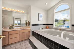 Bathroom featuring light tile patterned flooring, vaulted ceiling, double vanity, a jacuzzi tub, and recessed lighting