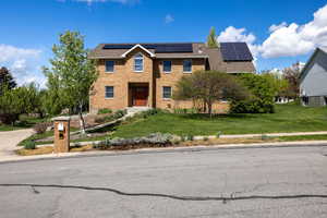 View of front of property with a front yard, solar panels, and brick siding
