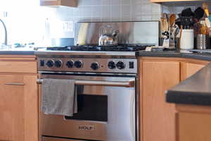 Kitchen featuring premium stove, tasteful backsplash, and dark countertops