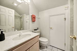 Bathroom featuring vanity, light tile patterned floors, vaulted ceiling, and a shower