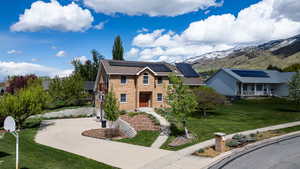 View of front of property featuring a front lawn, roof mounted solar panels, a mountain view, concrete driveway, and brick siding