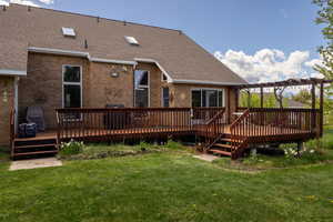 Rear view of house with roof with shingles, a wooden deck, brick siding, and a yard