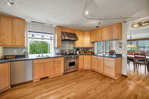 Kitchen featuring rail lighting, stainless steel appliances, light wood finish cabinets, a textured ceiling, and dark countertops