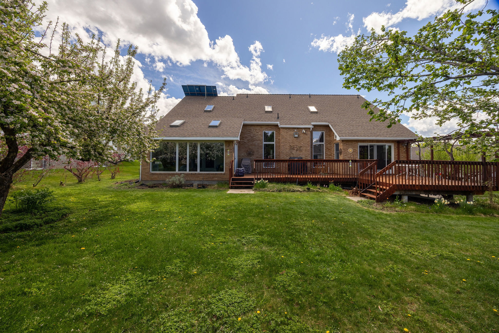 Rear view of property featuring a wooden deck, brick siding, a lawn, and a shingled roof