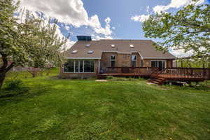 Rear view of property featuring a wooden deck, brick siding, a lawn, and a shingled roof