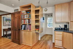 Kitchen featuring light wood finish cabinets, a textured ceiling, light wood-style floors, and dark Corian countertops
