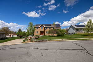 View of front of property featuring solar panels, a front lawn, brick siding, and a residential view