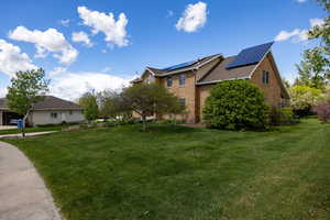 View of property exterior featuring a lawn, solar panels, and brick siding