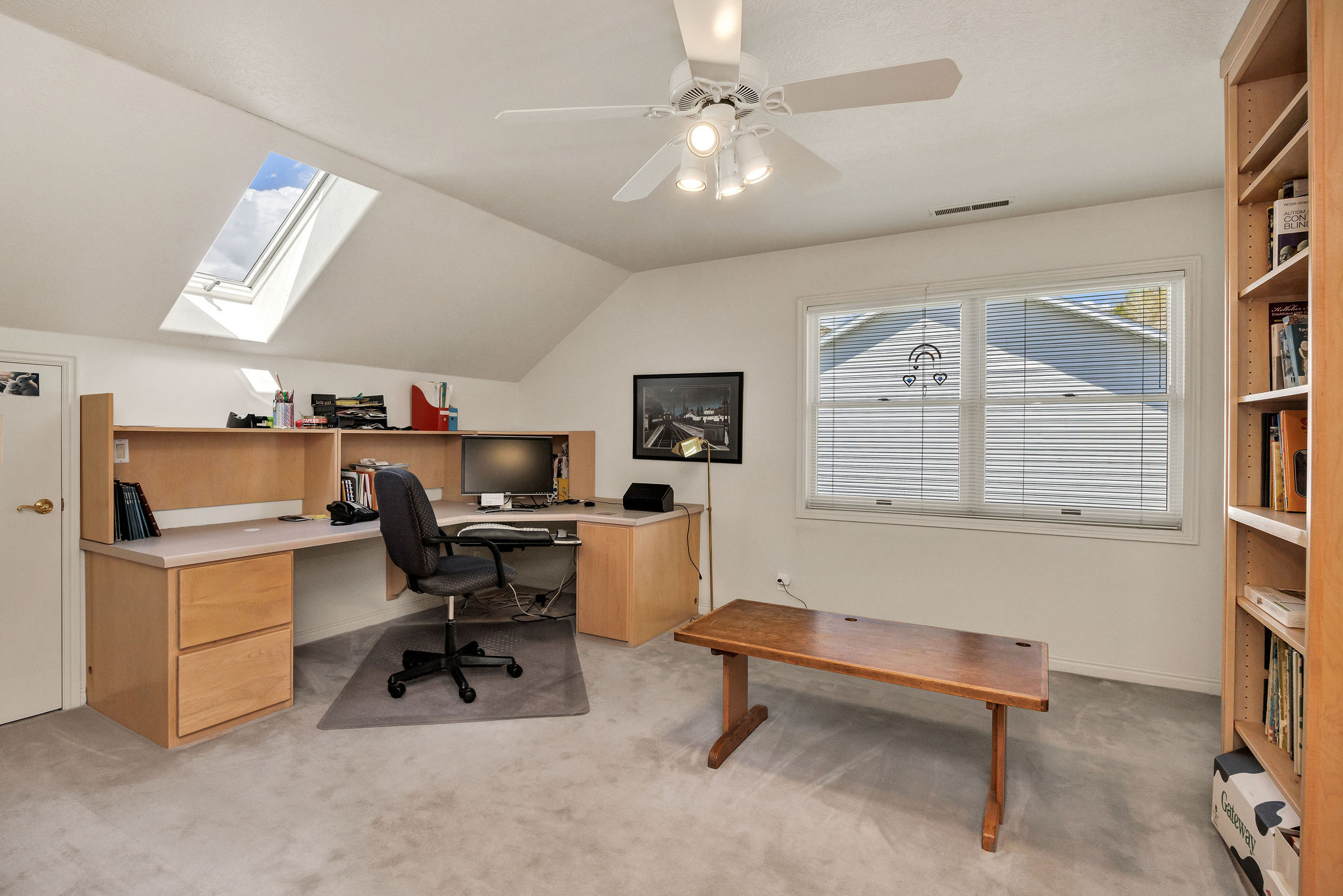 Office / bedroom area with ceiling fan, light carpet, vaulted ceiling, and a skylight