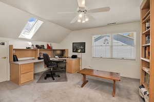 Office / bedroom area with ceiling fan, light carpet, vaulted ceiling, and a skylight