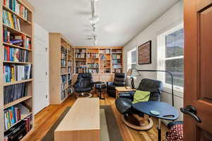 Den/ library featuring bookshelves, rail lighting, light wood finished floors, and built in shelves