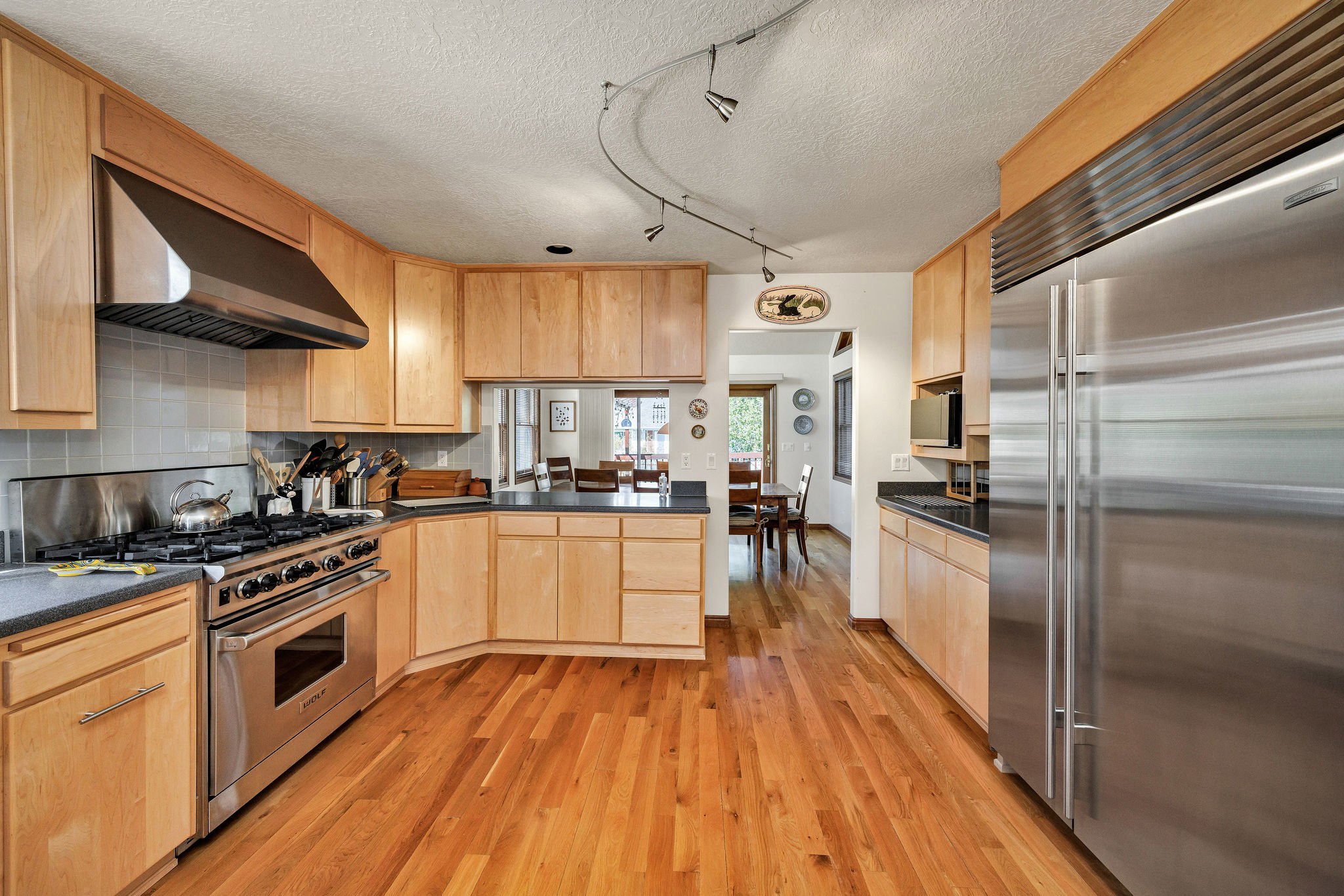 Kitchen featuring high quality appliances, rail lighting, range hood, light wood finish cabinetry, and light wood-style flooring