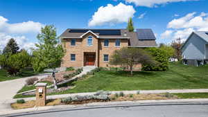 View of front of house with a front yard, roof mounted solar panels, brick siding, and a shingled roof