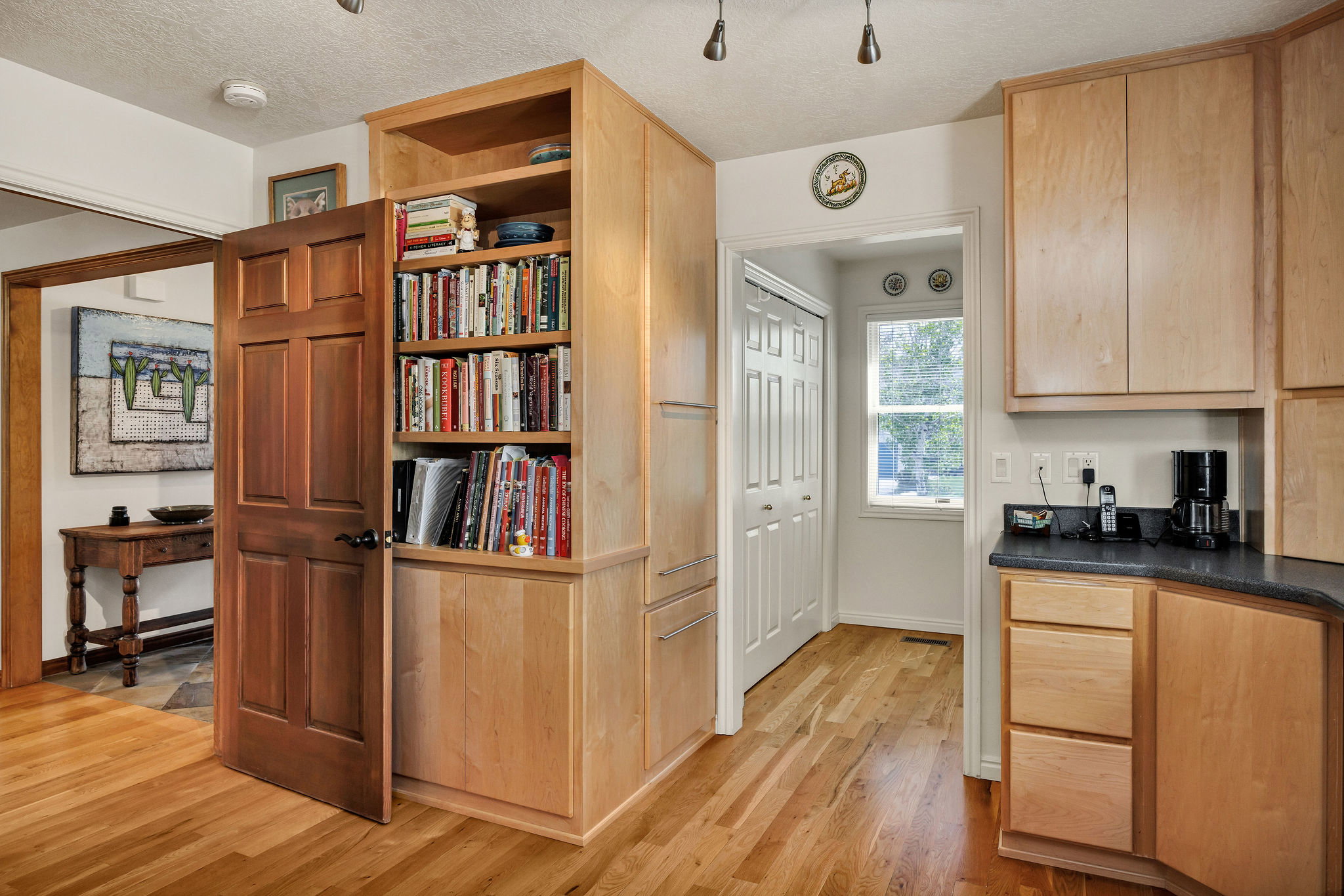 Kitchen with a textured ceiling, light wood finish cabinetry, dark countertops, light wood-type flooring, and open shelves