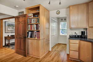 Kitchen with a textured ceiling, light wood finish cabinetry, dark countertops, light wood-type flooring, and open shelves