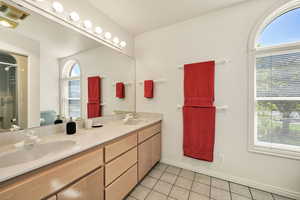 Full bath with double vanity, light tile patterned flooring, and a shower