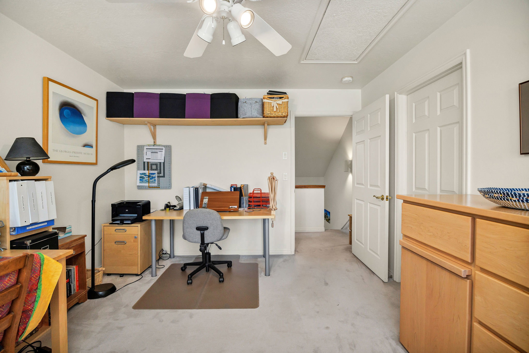 Office/ bedroom space with a ceiling fan, light colored carpet, and door to full bathroom