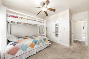 Carpeted bedroom with ceiling fan and a closet