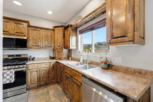 Kitchen featuring stainless steel appliances, wood finish cabinetry, dark stone finish floors, light countertops, and recessed lighting