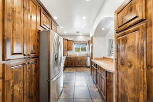 Kitchen featuring stainless steel refrigerator with ice dispenser, light countertops, recessed lighting, and wood finish cabinetry