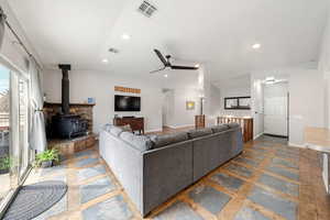 Living room featuring a wood stove, a ceiling fan, recessed lighting, and stone finish floors