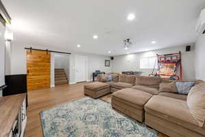 Living room with a barn door, light wood-style flooring, and recessed lighting